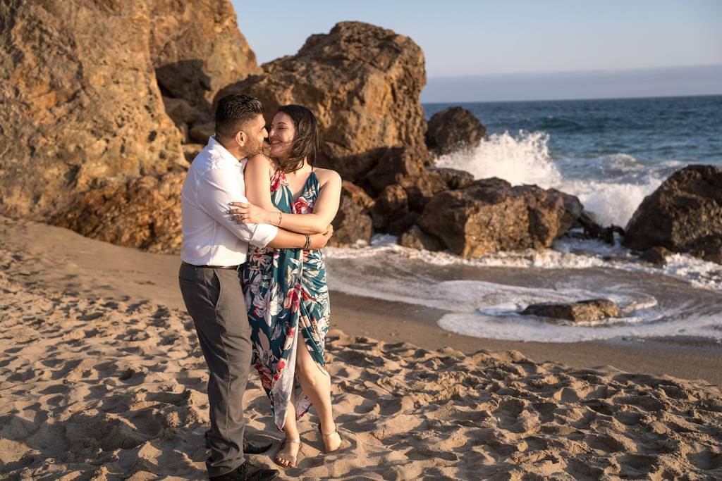 engagement couple hug by beach rocks