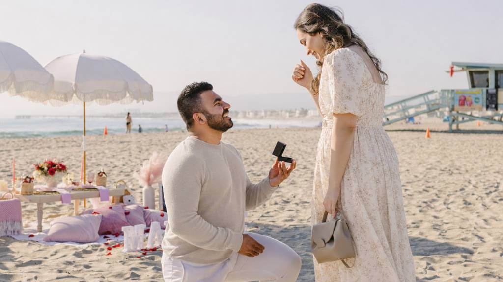 Man proposing during a beach picnic setup with light neutral outfits, soft decor, and ocean views for a romantic guide for proposals