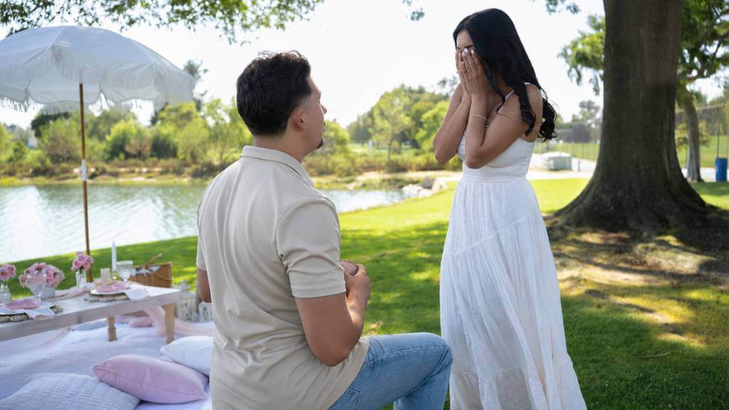 Lakeside garden proposal with picnic setup, white umbrella, soft neutral outfit, and romantic surprise moment for a guide for proposals