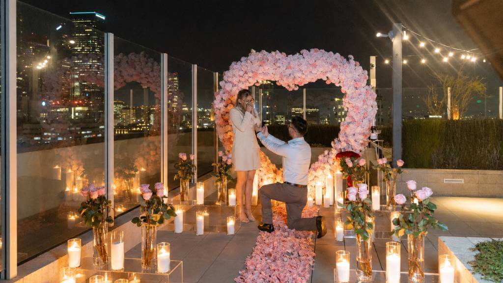 Rooftop proposal with candles, pink floral arch, city skyline, and elegant neutral outfits for a luxury guide for proposals